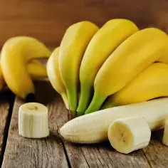 Pęczek żółtych bananów i kilka plasterków na drewnianym blacie. Zastanawiasz się, ile kalorii ma banan?
