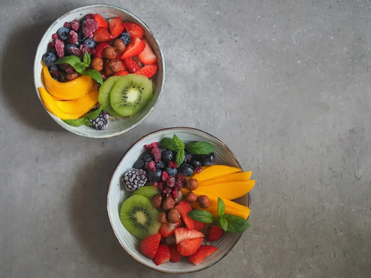 Dwa talerze owsianki z owocami: truskawkami, borówkami, malinami, jeżynami, kiwi, mango i orzechami. Czy owies ma gluten? Ten zdrowy posiłek jest bezglutenowy, jeśli użyjesz certyfikowanego owsa.
