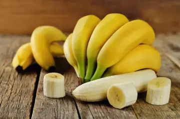 Pęczek żółtych bananów i kilka plasterków na drewnianym blacie. Zastanawiasz się, ile kalorii ma banan?